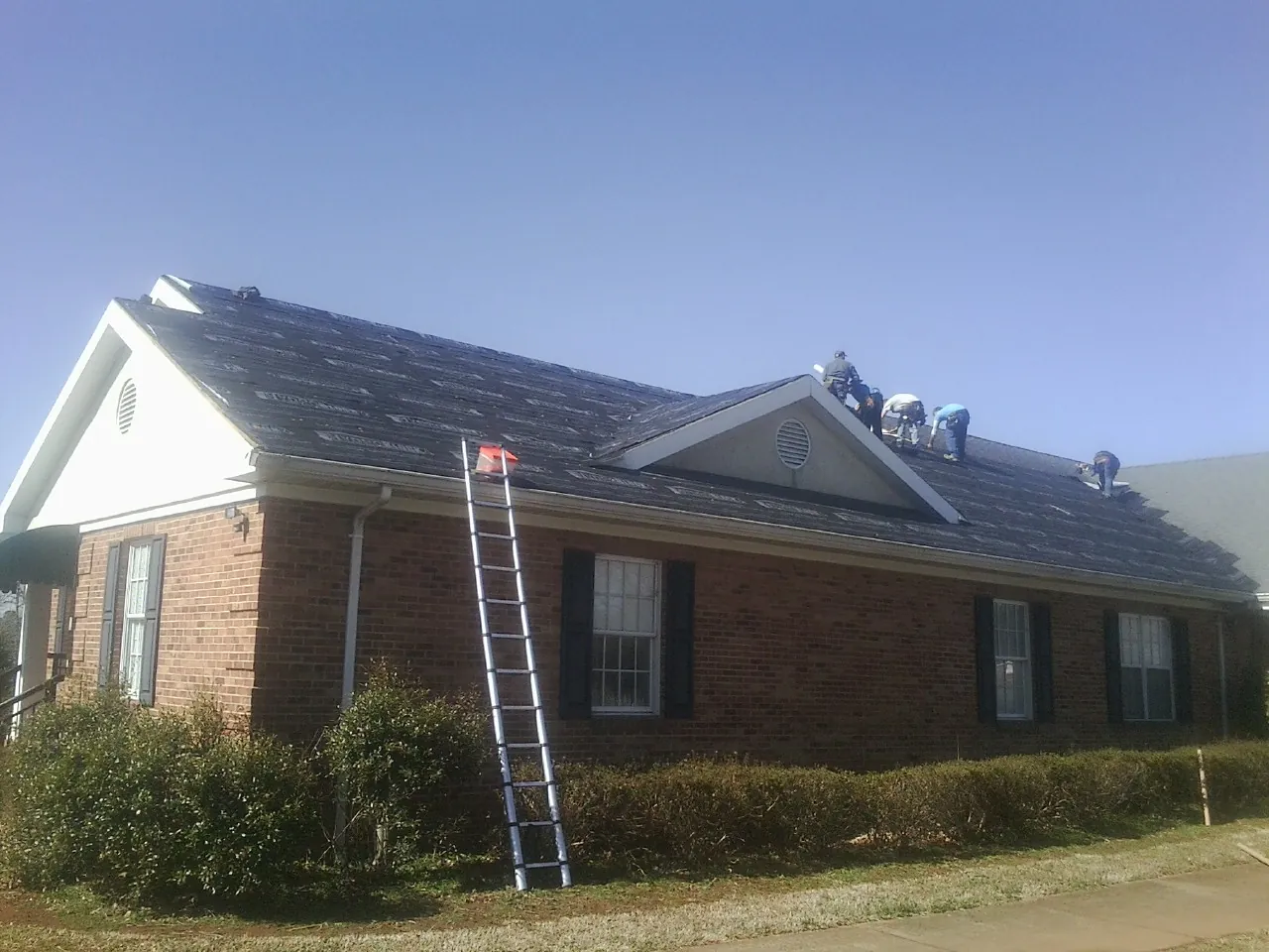 Crew tearing shingles off a brick ranch roof with a ladder set — Emergency Roof Repair work by our crew in Burlington