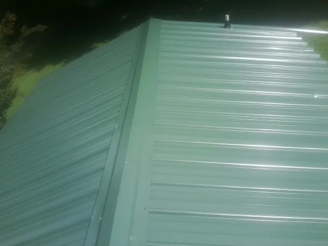 New green metal panels meeting at the ridge of a roof — Flat Roof Repair work by our crew in Burlington