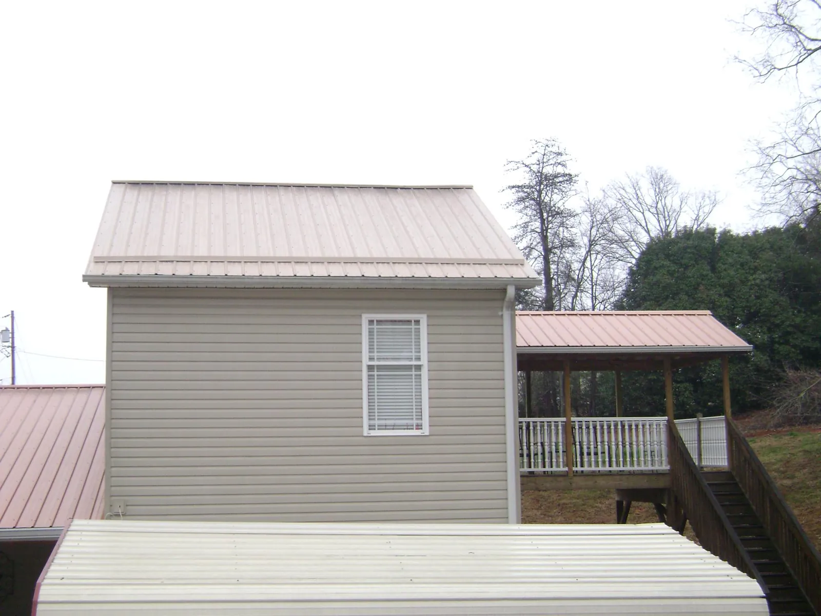 Tan metal roofs on a two story addition and attached porch, from a Roof Replacement job in Burlington